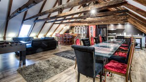 Un ampio loft con travi a vista in legno, una zona pranzo con tavolo in vetro e un angolo salotto accogliente con tavolino da calcio.