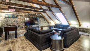 Un ambiente in stile loft con travi a vista in legno, parete in pietra, tavolo da calcio, un ampio divano modulare e una televisione a schermo piatto fissata al muro.