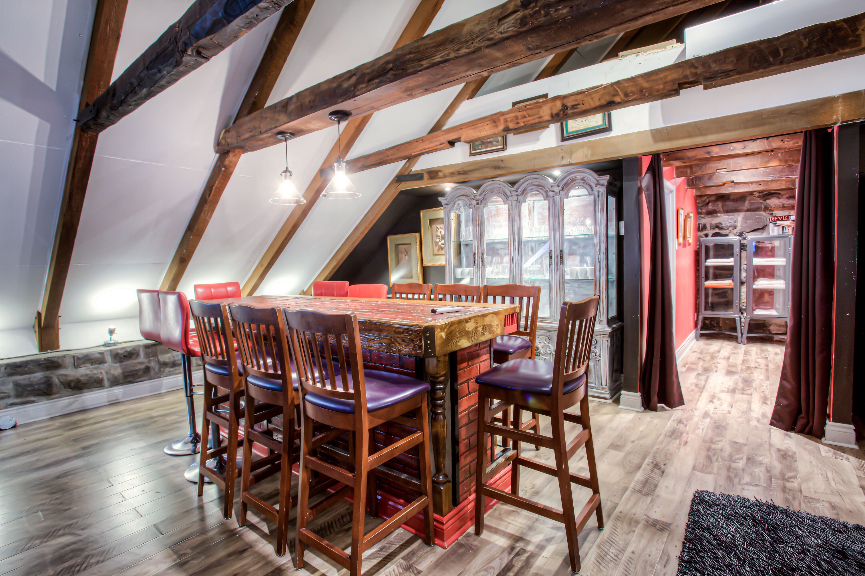 Un espace repas avec une table et des chaises en bois, un mur en pierre et un escalier menant à une autre pièce.