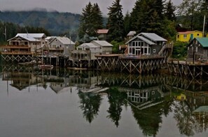 A waterfront property with multiple wooden houses on stilts, reflecting in calm water. - WATERFRONT COTTAGE RENTAL (Seldovia)