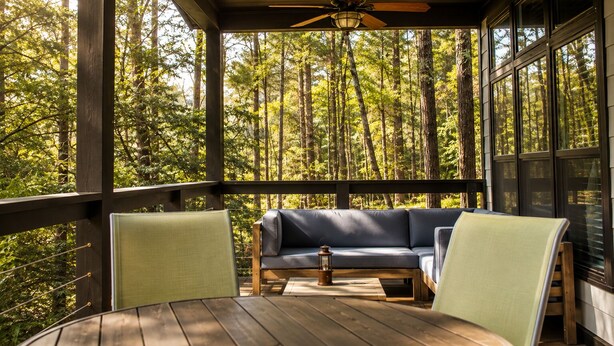 Terraza de madera con sofá y sillones, con vista a un bosque.