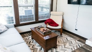 Un salón con un sofá blanco, una mesa de centro de madera con una bandeja de aperitivos, un plaid rojo en una silla y una alfombra estampada en patrón de espiga.