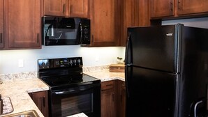 Una cocina con gabinetes de madera, un microondas negro, una estufa negra y un refrigerador negro.