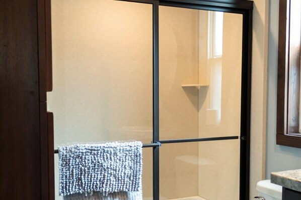 A bathroom with a glass shower enclosure, a towel hanging on a rack, and a marble countertop.