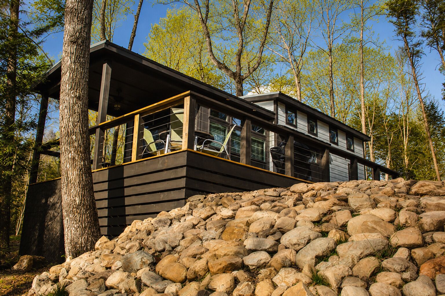 A modern cabin with a stone foundation, large windows, and a view of the surrounding forest.