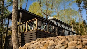 Una cabaña moderna con base de piedra, ventanas grandes y vistas al bosque circundante.