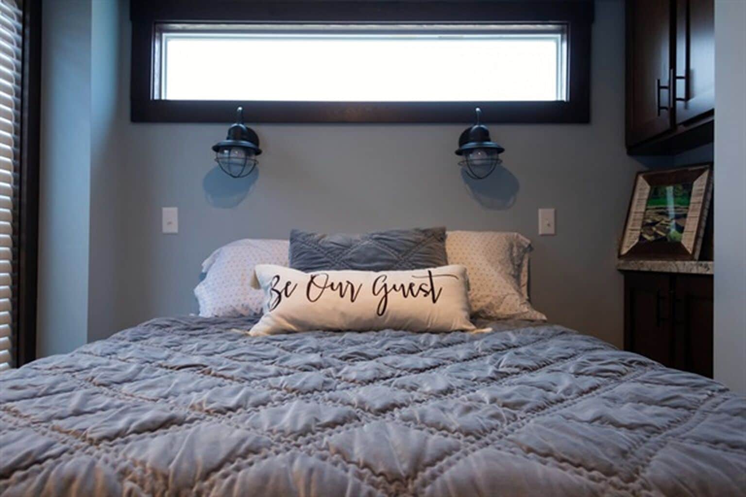 Un dormitorio con cama, dos lámparas de pared, una ventana y una almohada con texto.