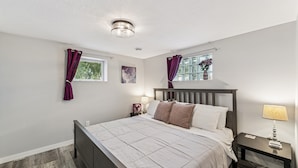 Un dormitorio con cama, mesita de noche, lámpara y ventana con cortinas.