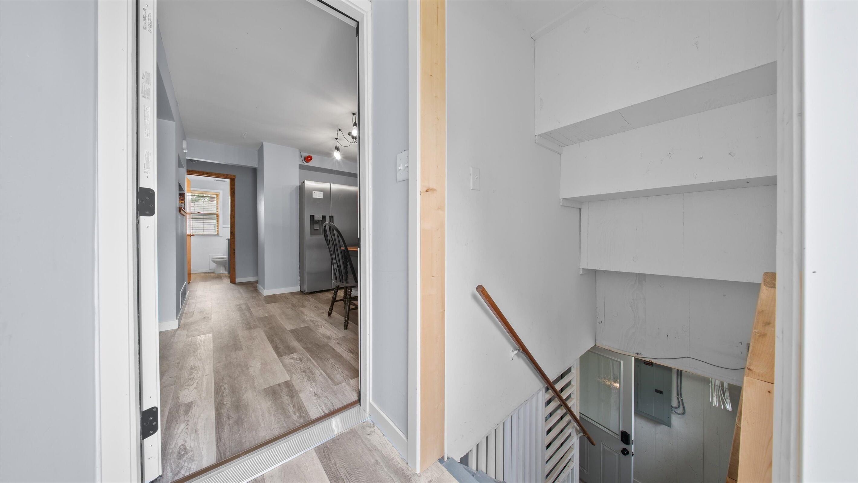 Un pasillo con piso de madera, una escalera con barandilla de madera y una pared blanca con una puerta.
