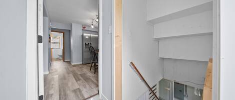 Un pasillo con piso de madera, una escalera con barandilla de madera y una pared blanca con una puerta.