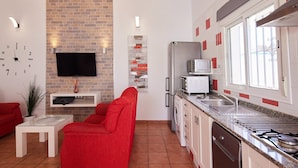 Une cuisine moderne équipée d’un four encastré, d’un micro-ondes et d’un lave-vaisselle. On y trouve un canapé rouge et une petite table avec une plante.