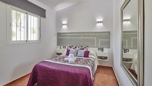 Une chambre à coucher avec un lit, des tables de chevet, un miroir et une fenêtre.