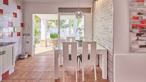 Une cuisine moderne avec des meubles blancs et un coin repas comprenant une table en verre et des chaises blanches.