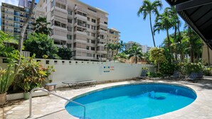 A swimming pool with a stone deck, surrounded by potted plants and lounge chairs. - Spacious 2br Waikiki (Honolulu)