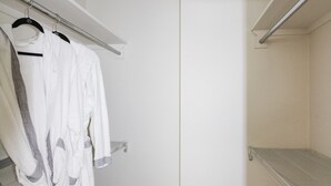 A walk-in closet with white robes hanging on a rack, a white shelf, and a beige carpet. - Spacious 2br Waikiki (Honolulu)