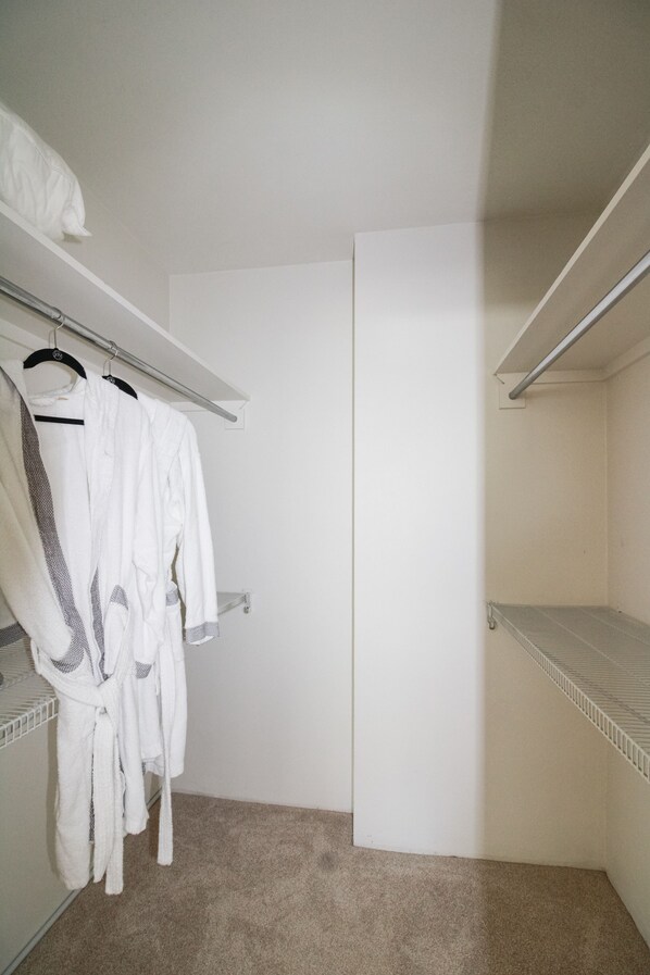 Vestidor con batas blancas colgadas en un perchero, un estante blanco y una alfombra color beige.