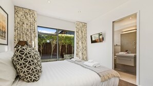 Une chambre à coucher moderne, dotée d’un grand lit, d’un téléviseur fixé au mur et d’une salle de bain visible à travers une porte ouverte.