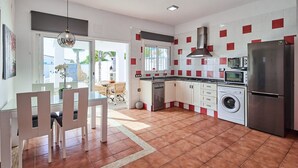 A modern kitchen with a washing machine, a refrigerator, and a dining area with chairs and a table. - Villa Yuca Conil de la Frontera by Ruralidays (Cádiz)