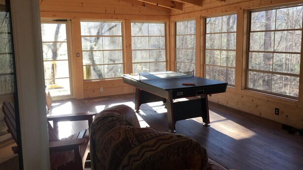 A spacious room with a pool table, large windows, and wooden walls.