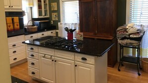 A kitchen with white cabinets, a black countertop, and a wooden island. There are two wooden cabinets with decorative chickens on top.