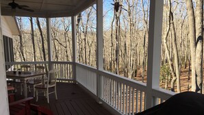 A covered porch with a table and chairs, overlooking a forested area.