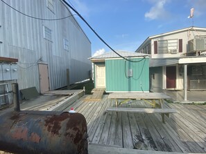 A wooden deck with a metal structure, a green shed, and a building with a red door. - R&R Getaway Comfort on the water! (Venice)