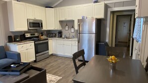 A modern kitchen with white cabinets, a stainless steel refrigerator, and a dining table with chairs.