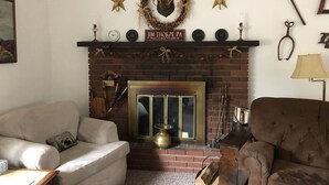 A cozy living room with a fireplace, a mantel decorated with stars and a wreath, and a rustic wooden chair. - Jim Thorpe minutes away! Cozy Cabin, Peace & Quiet in Private Lake Community! (Jim Thorpe)