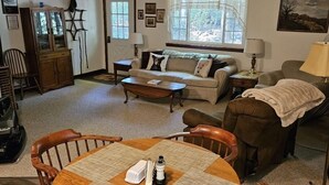 A cozy living room with a round wooden table, two sofas, a cabinet, and a window with a view of trees. - Jim Thorpe minutes away! Cozy Cabin, Peace & Quiet in Private Lake Community! (Jim Thorpe)