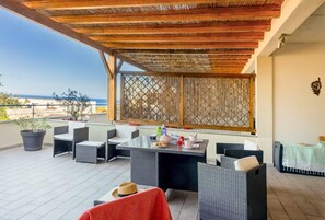 A covered outdoor seating area with wicker furniture, a table with drinks, and a view of the sea. - Casa Balanina (Lumio)