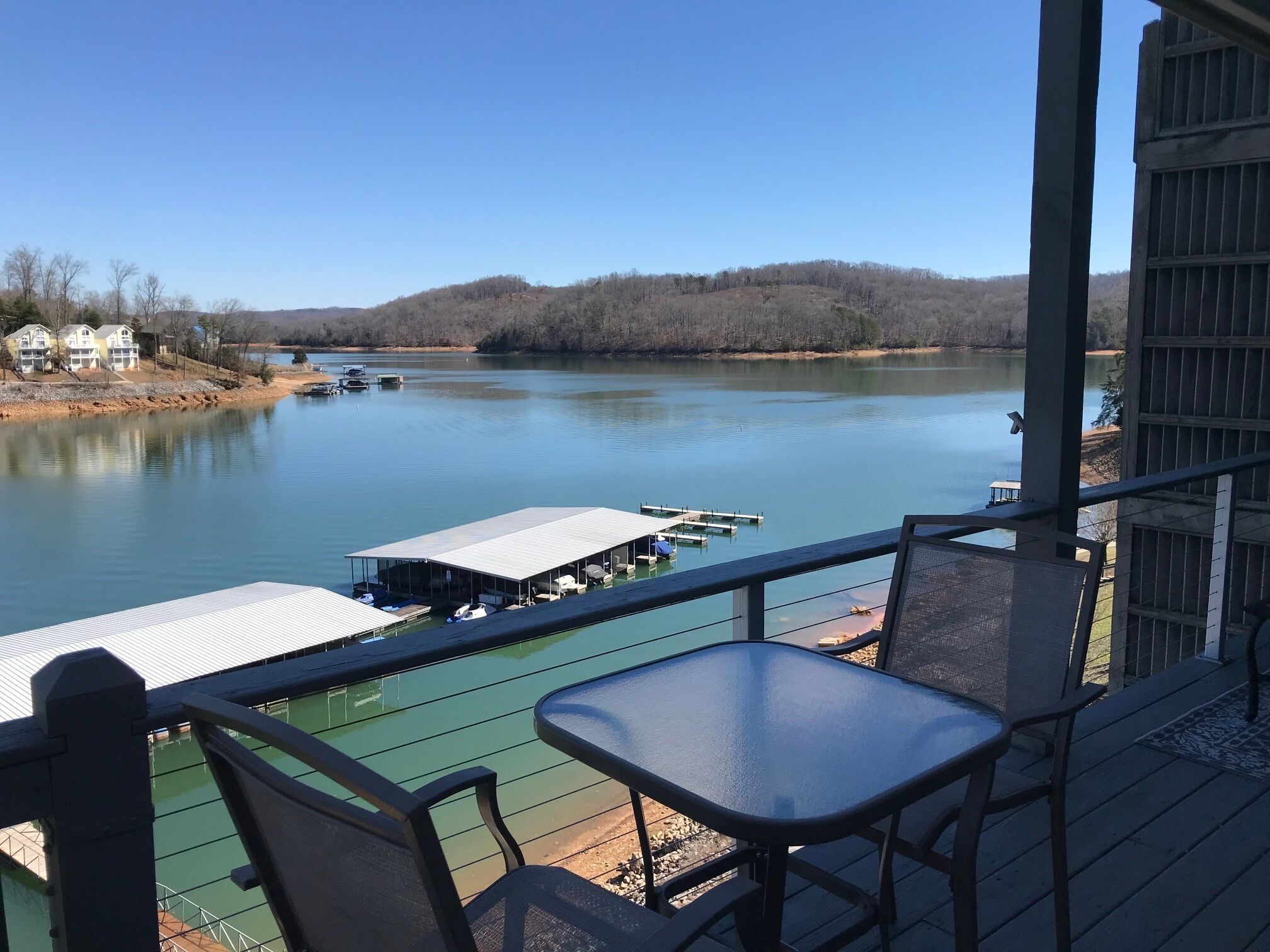 A balcony with a view of a calm lake, docked boats, and a distant hill.