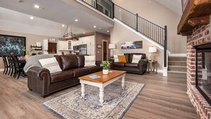 A spacious living room with a brown leather sofa, a wooden coffee table, and a large rug. A staircase leads to an upper level with a view of the kitchen. - Putting Green,  Lakeviews, Indoor Pool,Pickleball (Branson)