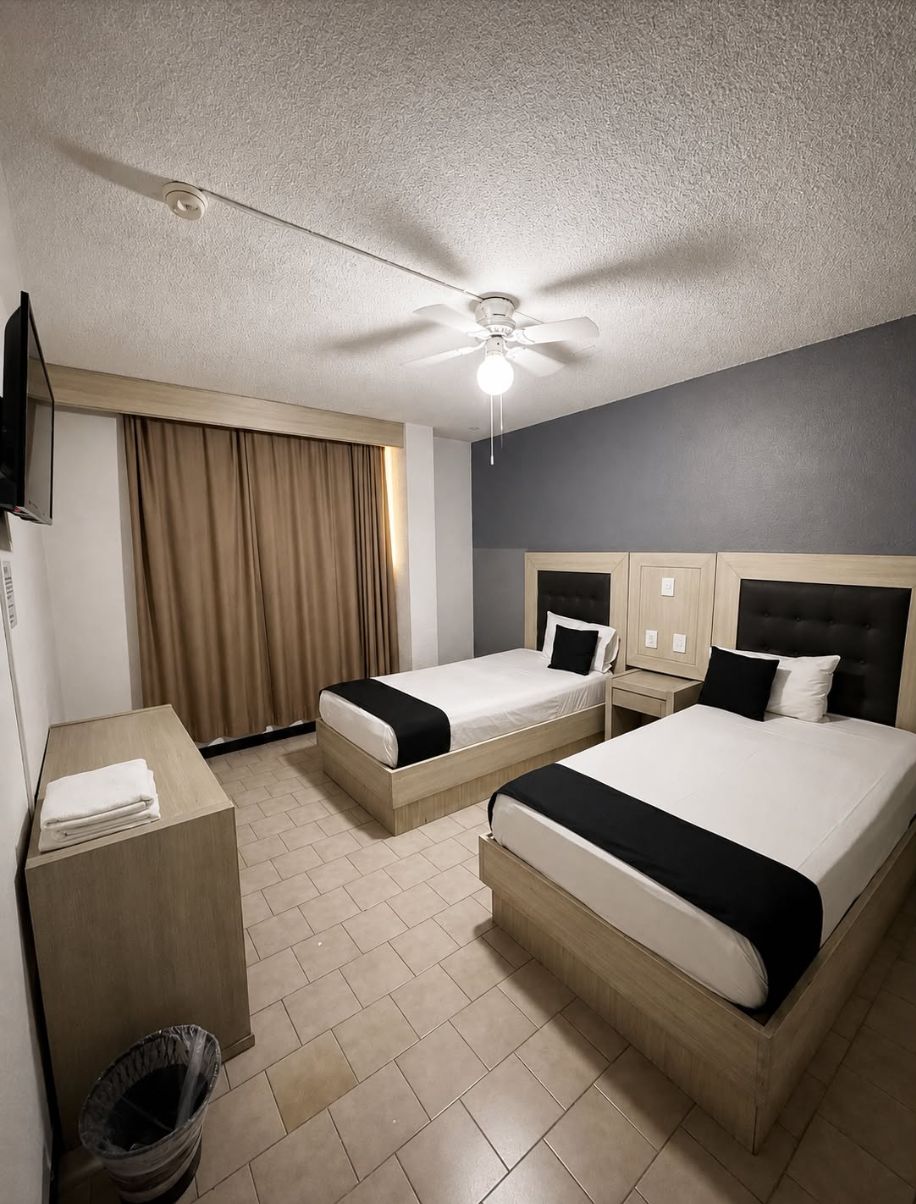 A hotel room with two beds, a ceiling fan, a TV, and a window with curtains.