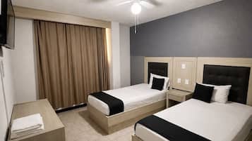 A hotel room with two beds, a ceiling fan, a TV, and a window with curtains.