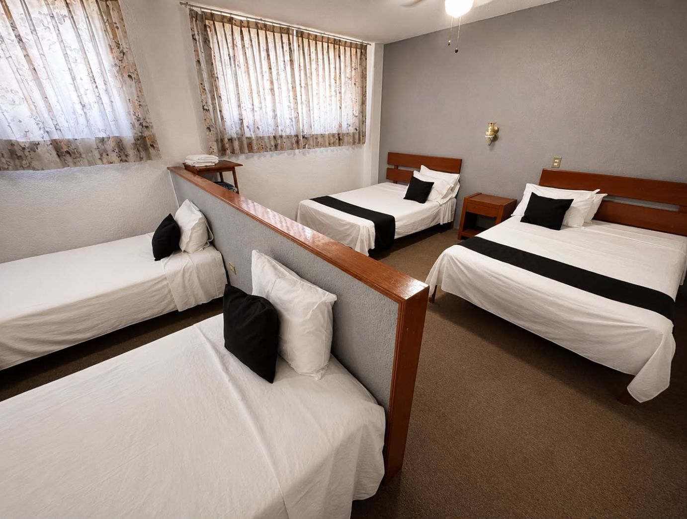 A hotel room with four single beds, a wooden headboard, a small table, and a nightstand.