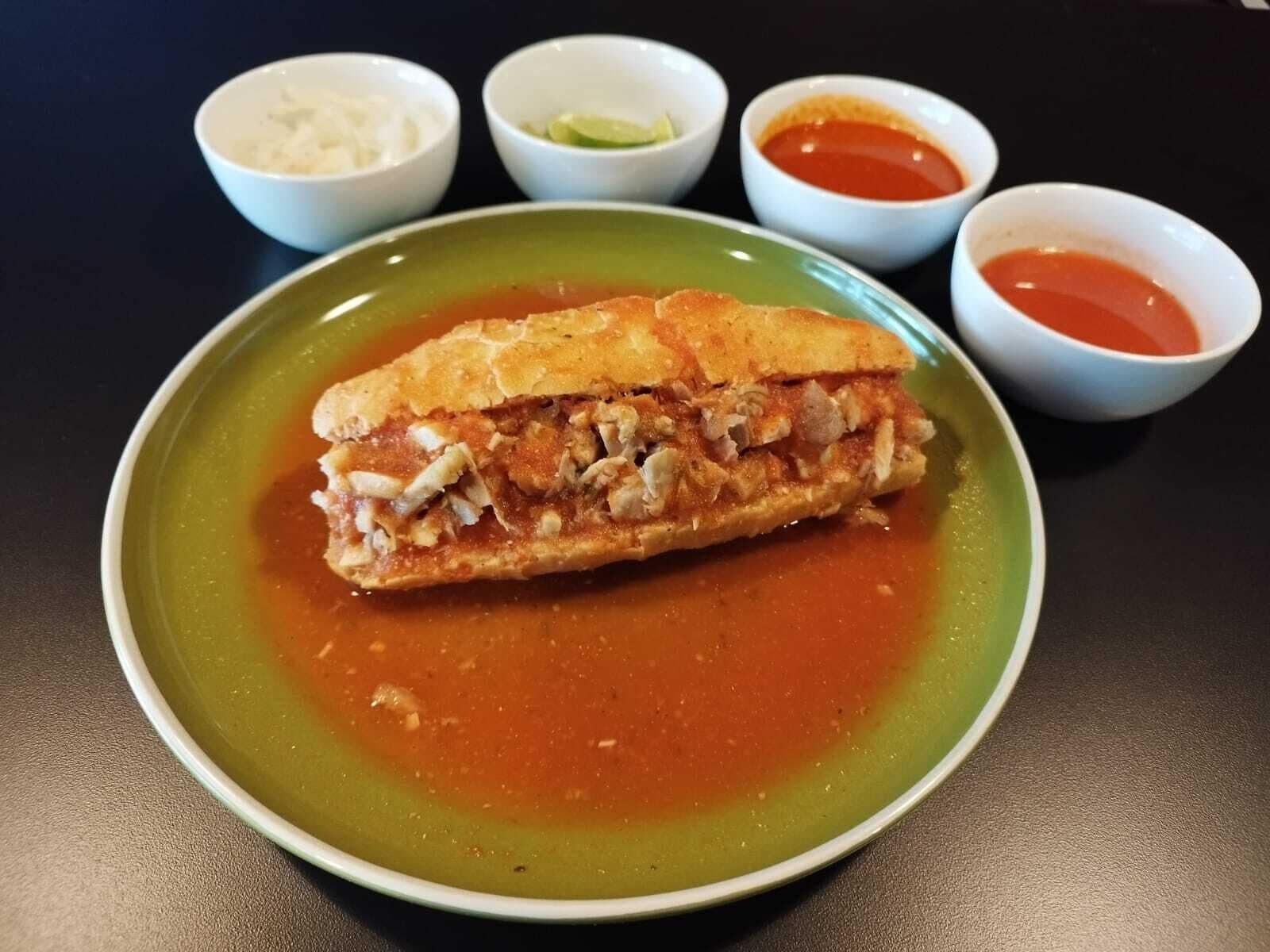 A sandwich on a green plate with a side of sauce.