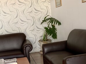 A room with two leather sofas, a patterned wallpaper, a potted plant, and a framed picture on the wall. - Hotel Italia Aguascalientes (Aguascalientes)