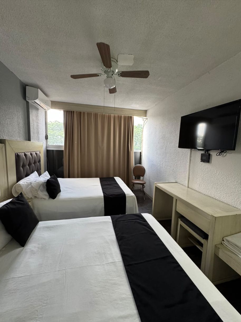 A hotel room with two beds, a ceiling fan, a TV, and a desk.