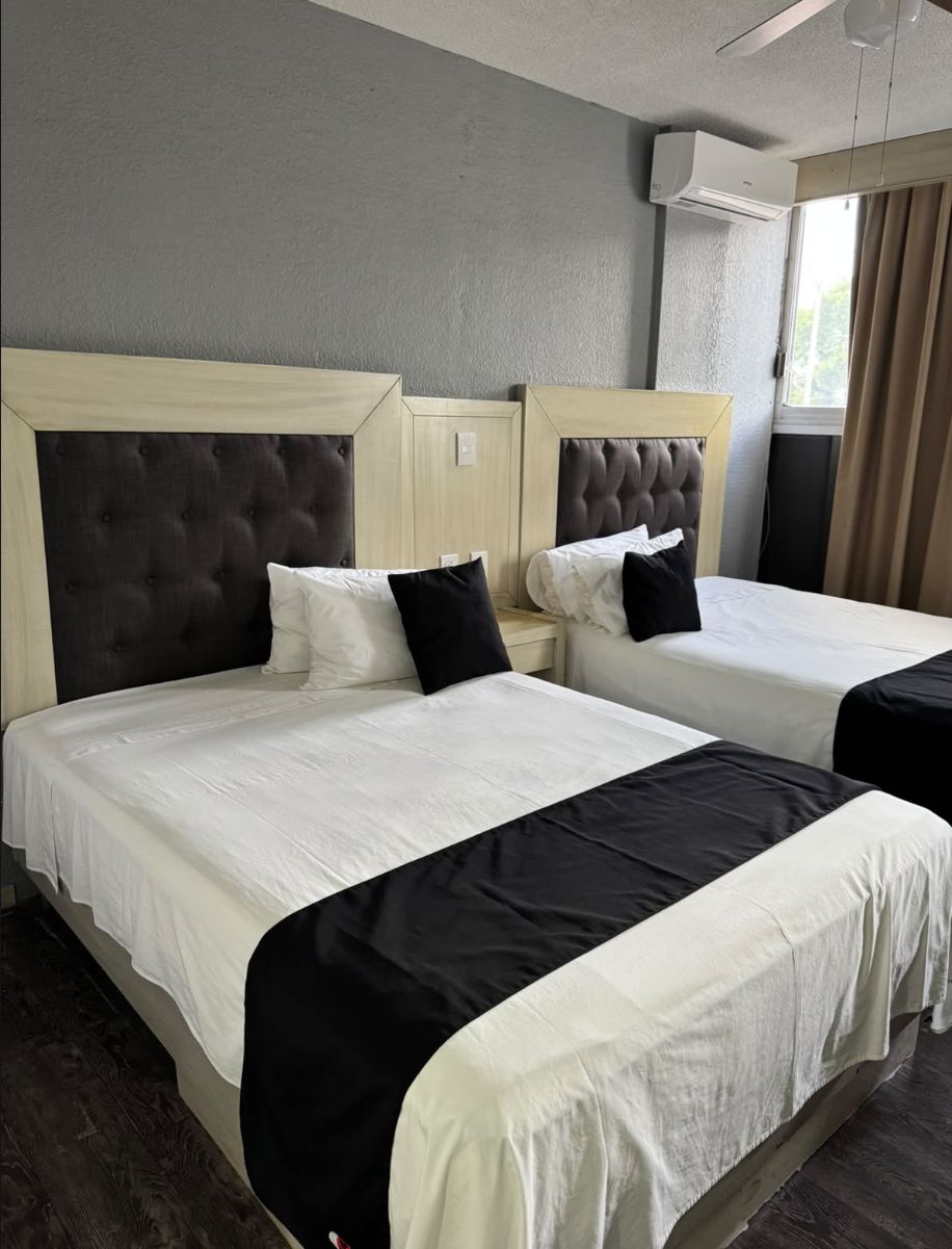 A hotel room with two beds, each with a headboard, white bedding, and black accent pillows.