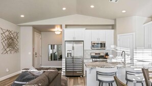 A modern kitchen with white cabinets, stainless steel appliances, and a central island with bar stools. - The Haven - Great location! Pickleball! (Washington)