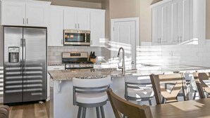 A modern kitchen with white cabinets, stainless steel appliances, a granite countertop, and bar stools. - The Haven - Great location! Pickleball! (Washington)