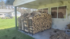 A covered porch with a stack of firewood and a grill area. - Connors Lake Landing - Home/Hangar & Federal License Grass Runway - 2WS2 (Webster)