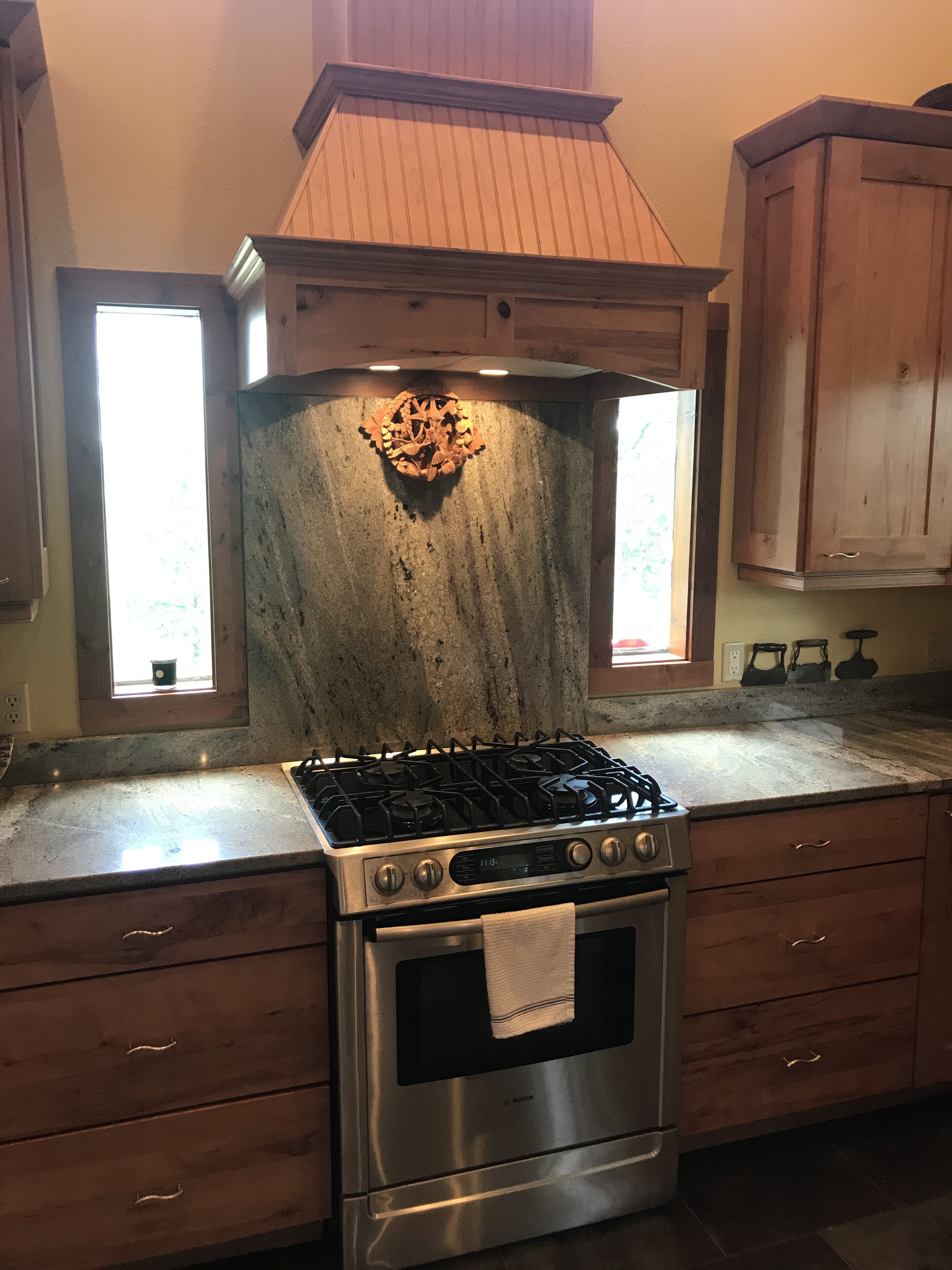Une cuisine équipée d’une cuisinière à gaz Bosch, de meubles de rangement en bois et d’un pare-feu en pierre.