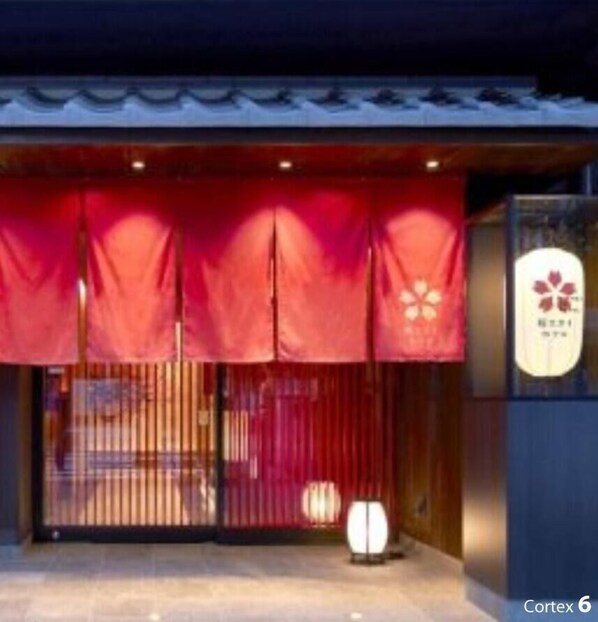 Entrada de un edificio con toldo rojo, puerta de vidrio y un letrero con un logotipo de flor.