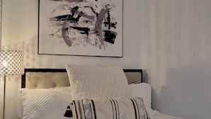 Une chambre à coucher avec un lit, une lampe de chevet et un tableau abstrait accroché au mur.
