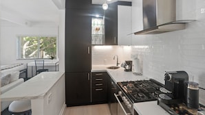 Une cuisine moderne avec des meubles de rangement de couleur sombre, un plan de travail blanc, une cuisinière à gaz et une machine à café.