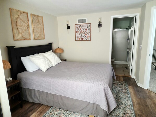 A bedroom with a bed, a nightstand, a lamp, two wall art pieces, and a bathroom door.