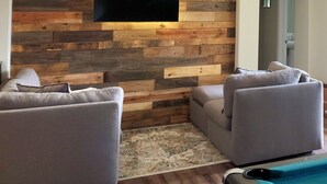 Ein Wohnzimmer mit Holzpaneelen, zwei grauen Sofas, einem kleinen Couchtisch und einem an der Wand befestigten Flachbildfernseher.