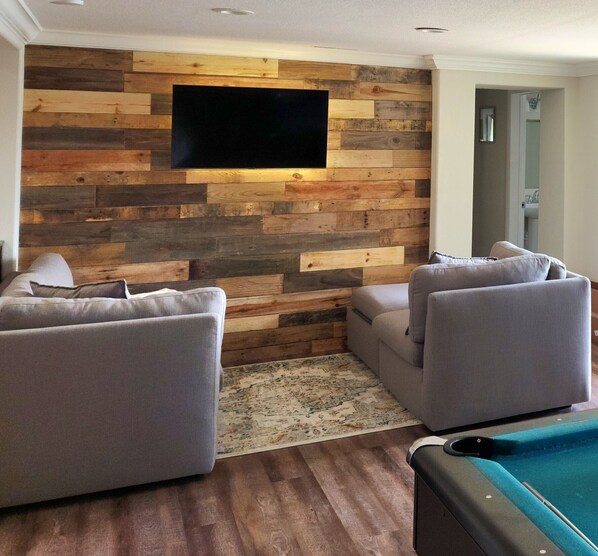 Una sala de estar con un panel de pared de madera, dos sofás grises, una pequeña mesa de centro y un televisor de pantalla plana montado en la pared.