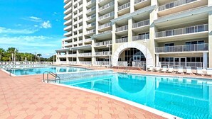 Un hotel con un amplio área de piscina, varios balcones y un cielo azul despejado.